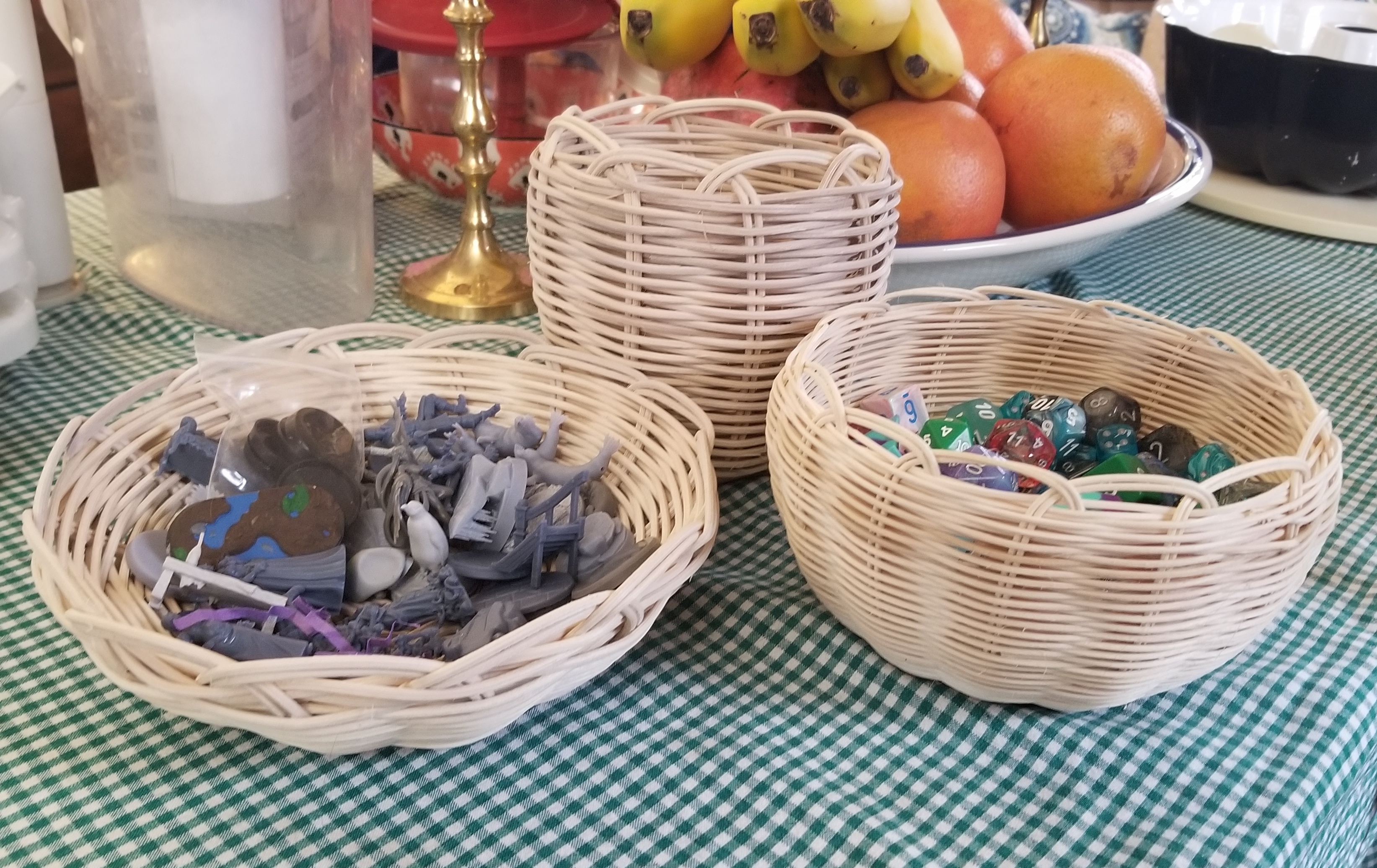 Three natural reed baskets, one shallow filled with unpainted miniatures, one medium sized filled with dice, and one empty taller basket.