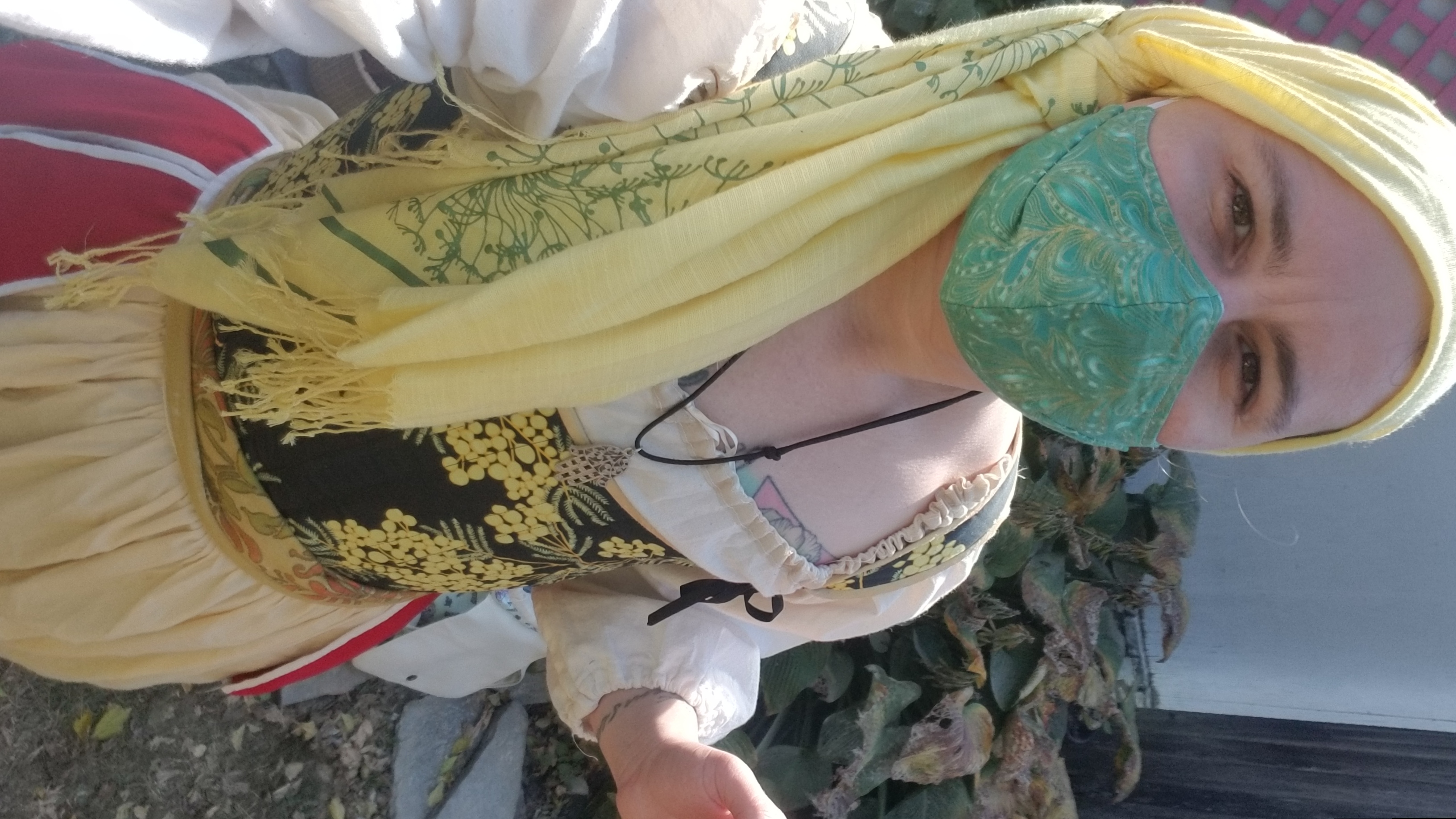 Thomas, at a Renaissance Faire in 18th century dress, with wattle patterned stays, a skirt with the pockets worn on top, and a head scarf.