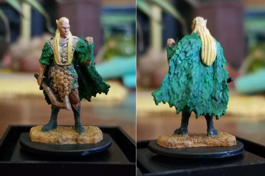 A tan skinned elf with long blond hair, in a green cloak made of leaves and armor of green, gold and silver.